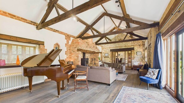 A spacious living room with a grand piano, a stone fireplace, and a large window providing natural light. - Host Stay The Old Foundry (King's Lynn)