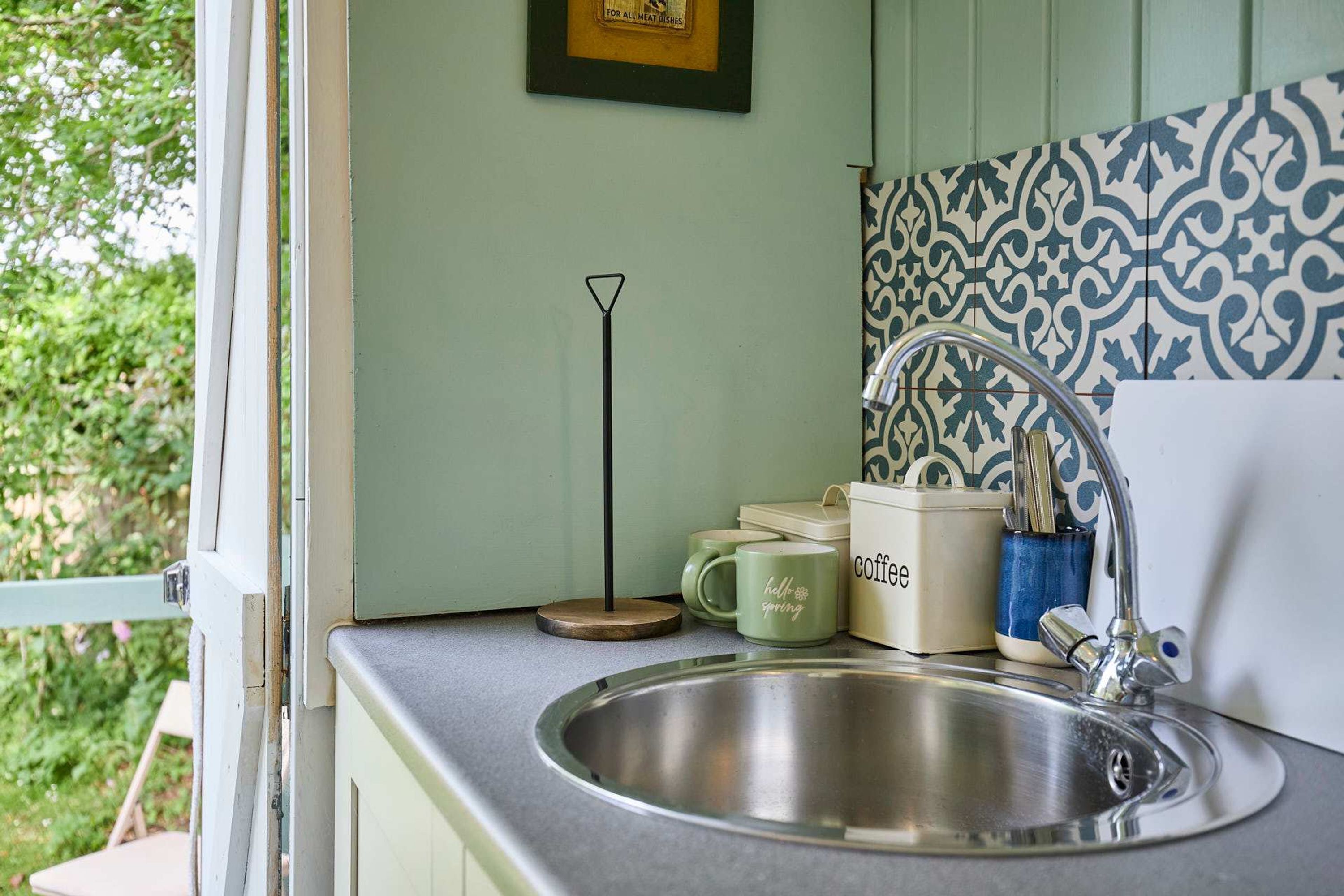 A kitchen with a stainless steel sink, a coffee maker, and a patterned backsplash.