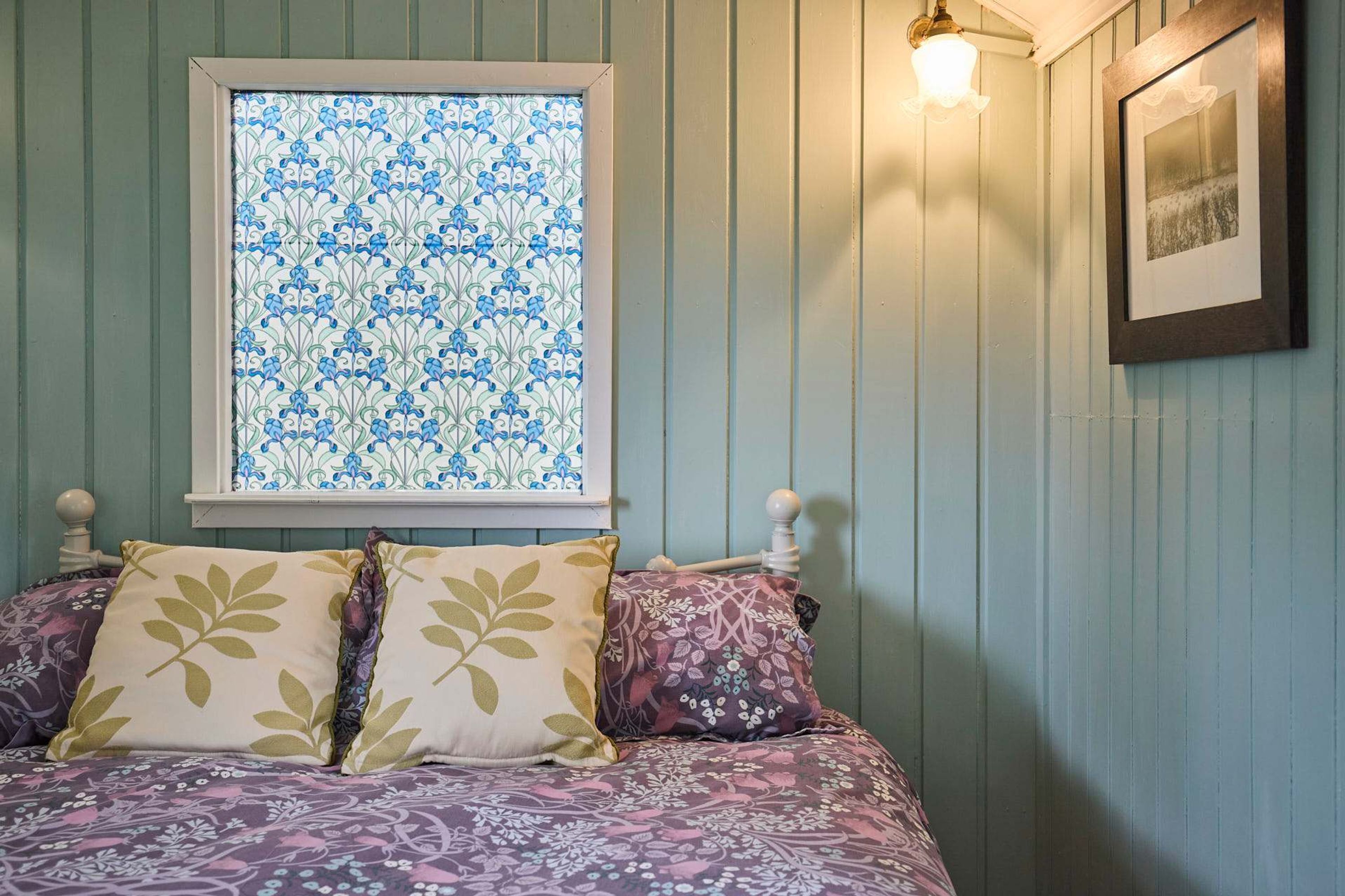 A bedroom with a bed, a window with a blue and white pattern, and a wall-mounted light fixture.