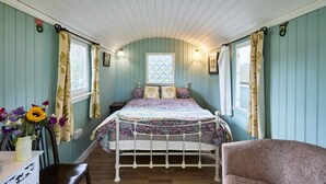 A cozy bedroom with a bed, a chair, and a table with a vase of flowers.
