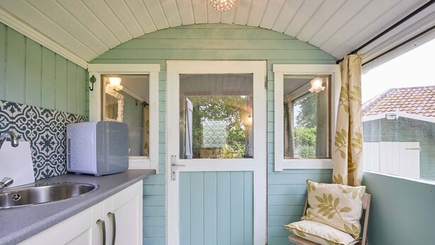 A compact kitchen with a sink, a microwave, and a chair with a cushion.