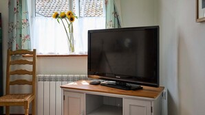 A room with a wooden desk, a television, a chair, and a window with sunflowers. - Host Stay The Lodge (Melton Constable)