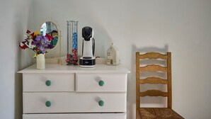 A white dresser with teal knobs, a coffee maker, a vase with flowers, a mirror, and a wooden chair. - Host Stay The Lodge (Melton Constable)