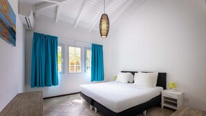 A bedroom with a bed, a nightstand, a lamp, and a window with curtains. - Spanish Water Marina Triple Penthouse (Jan Thiel)