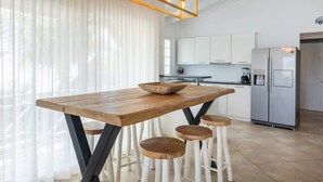 A modern kitchen with a wooden table, stools, and a stainless steel refrigerator. - Spanish Water Marina Triple Penthouse (Jan Thiel)