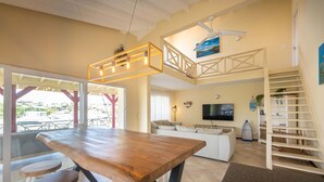 Amplia sala de estar con mesa de comedor de madera, sofás blancos y televisor.