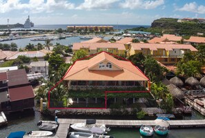 Un hotel frente al mar con techo de tejas rojas, zona de piscina y un puerto deportivo con barcos.