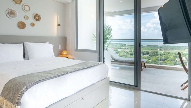 Un dormitorio moderno con una cama grande, un balcón con vistas y detalles decorativos en la pared.