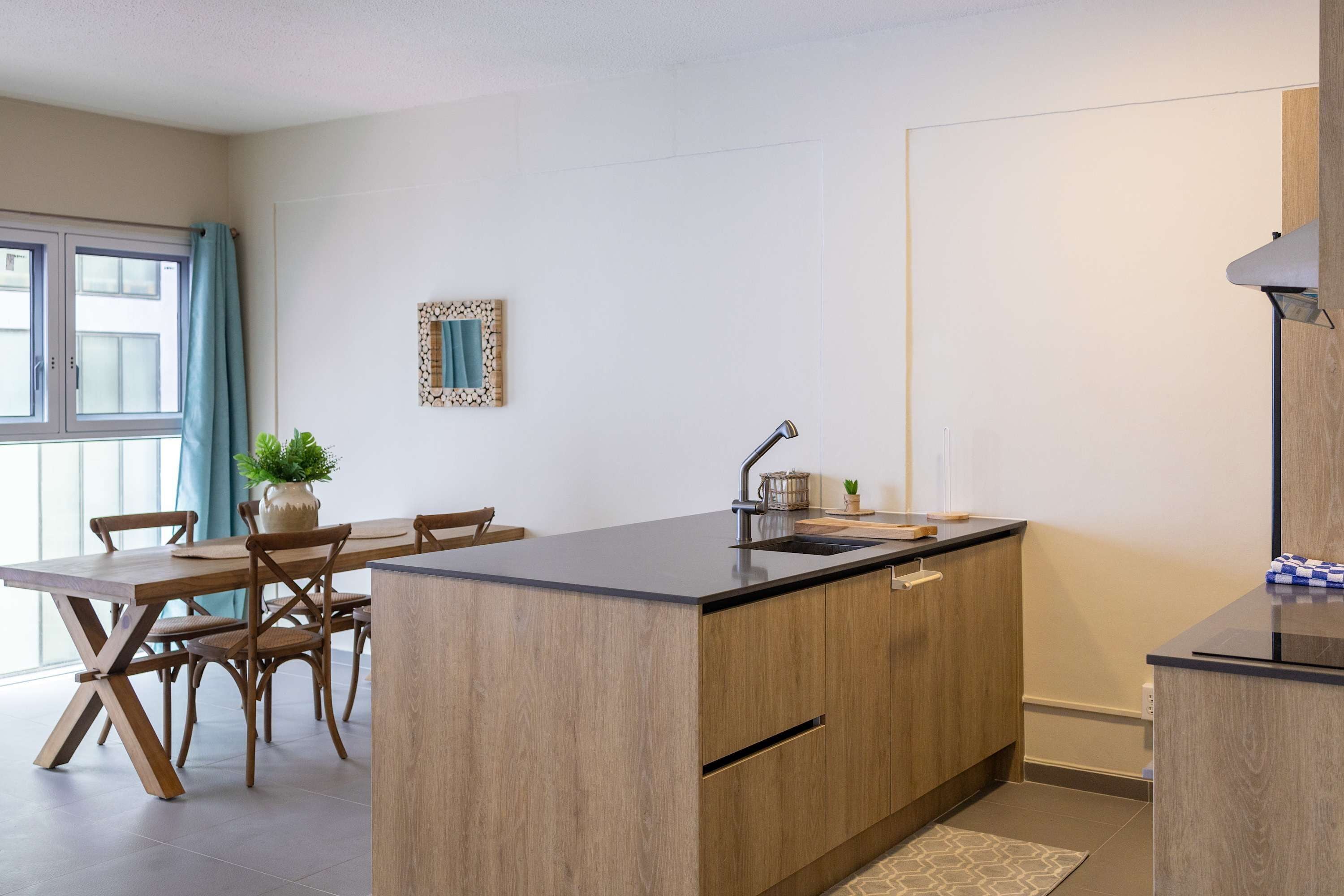 Une cuisine moderne avec un îlot central en bois, une table à manger avec des chaises et une fenêtre agrémentée de rideaux.