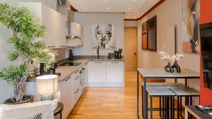A modern kitchen with white cabinets, a central island, and a dining area with a table and benches. - The Honourable - Bloomsbury Square By Frankie Says (London)