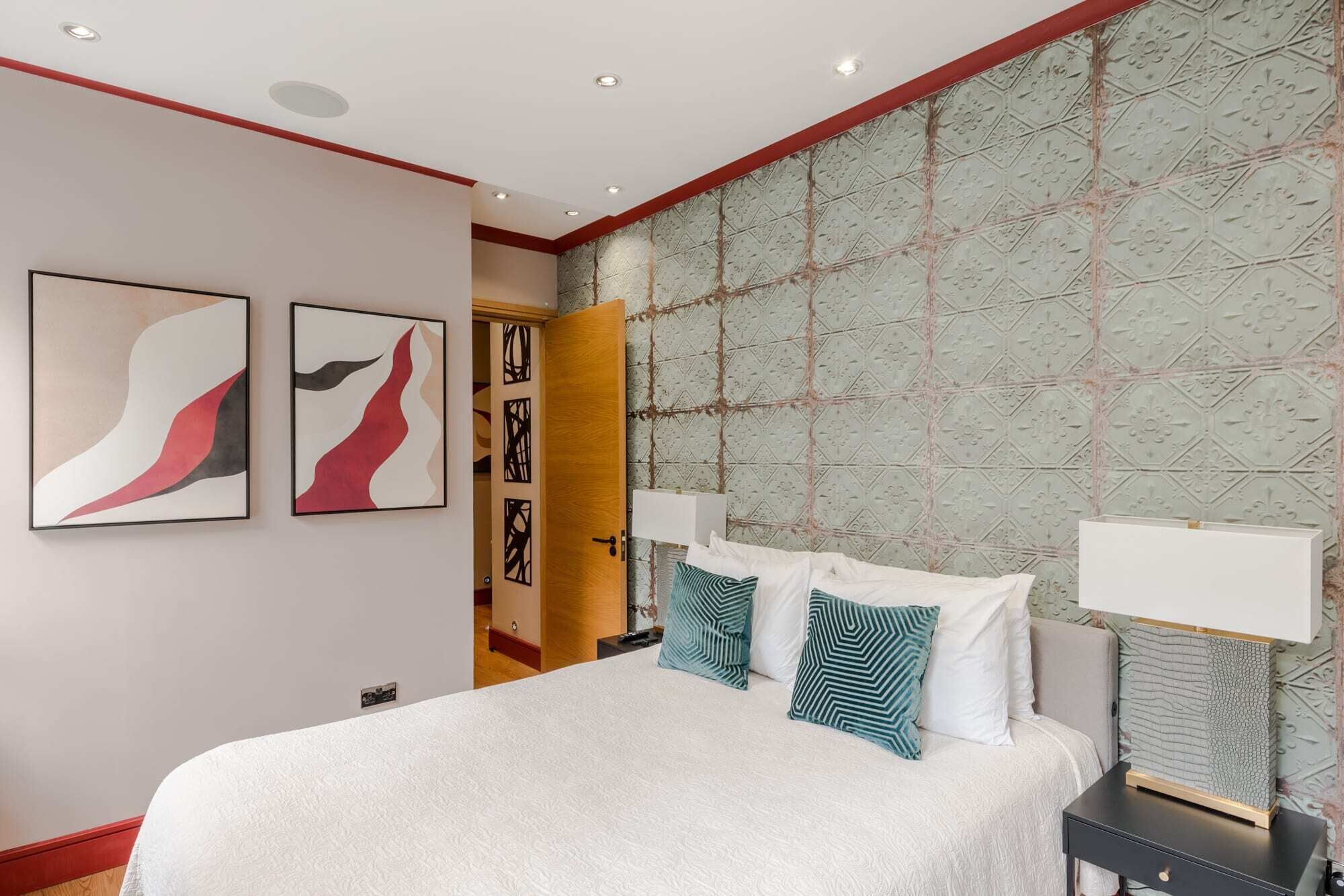 A hotel room with a large bed, two wall-mounted lamps, and abstract art on the walls.