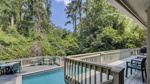 A pool area with a wooden deck, surrounded by dense forest.