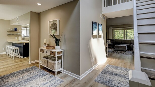 A spacious living area with a high ceiling, a staircase, and a kitchen area with bar stools.