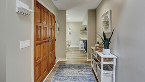 A hallway with a wooden door, a white console table with a plant, and a blue rug.
