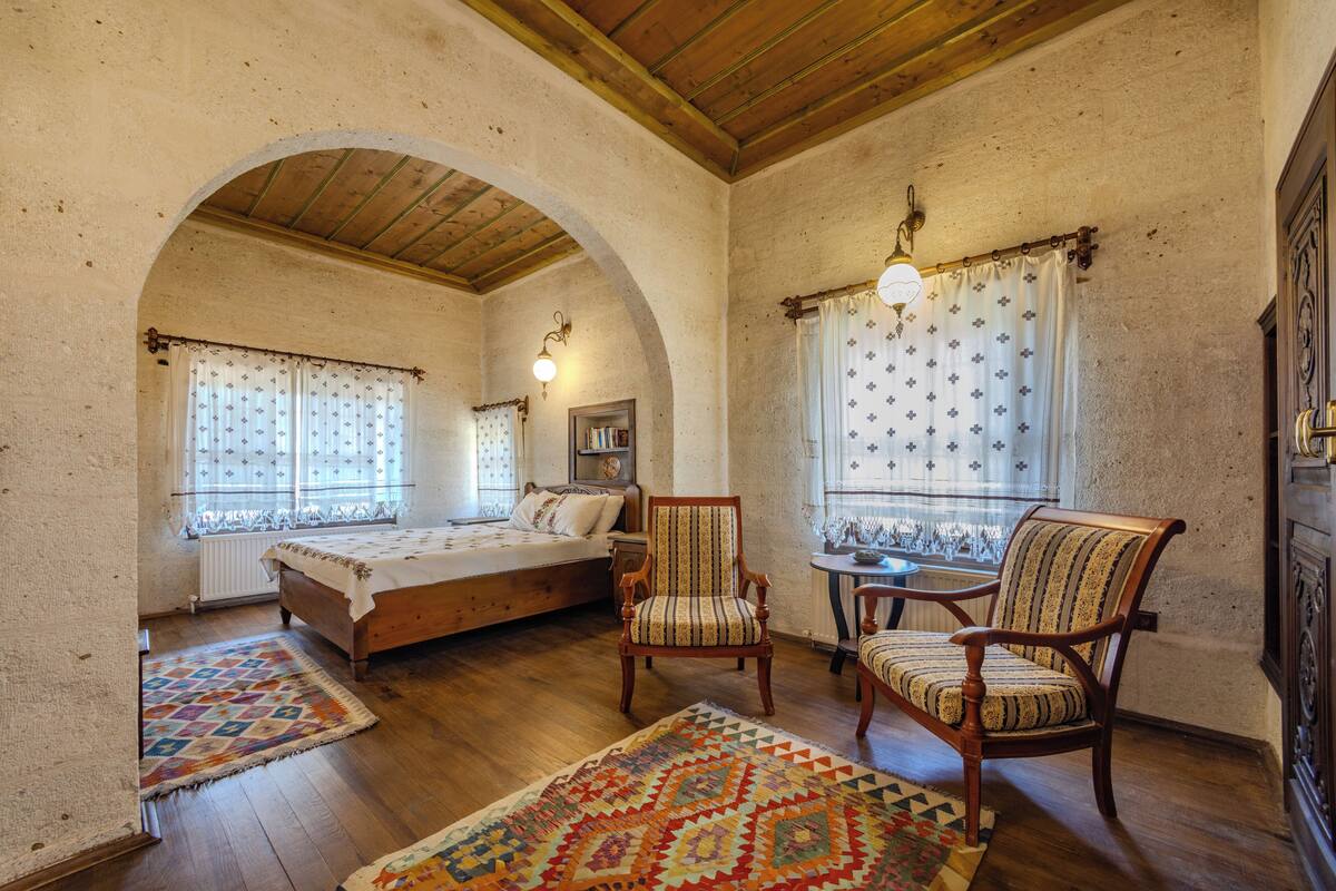 Ein gemütliches Schlafzimmer mit einem Holzbett, zwei Stühlen, einem kleinen Tisch und einem gemusterten Teppich.
