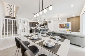 Een moderne eethoek met een witte tafel voor vier personen, zwarte stoelen en een keuken op de achtergrond.