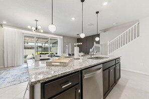 A modern kitchen with a granite countertop, stainless steel appliances, and pendant lighting.