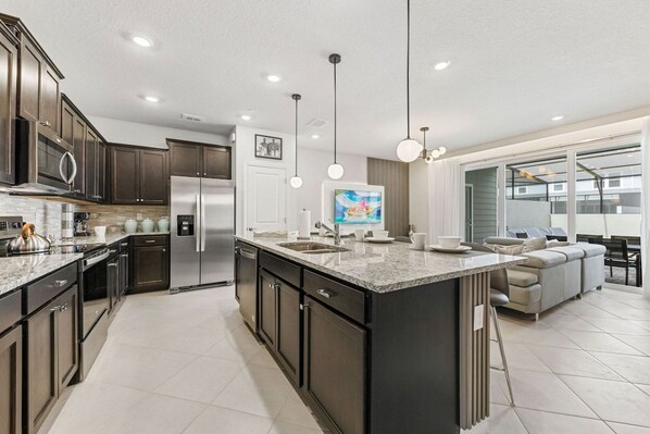 A modern kitchen with dark cabinetry, stainless appliances, and a large island with a sink.
