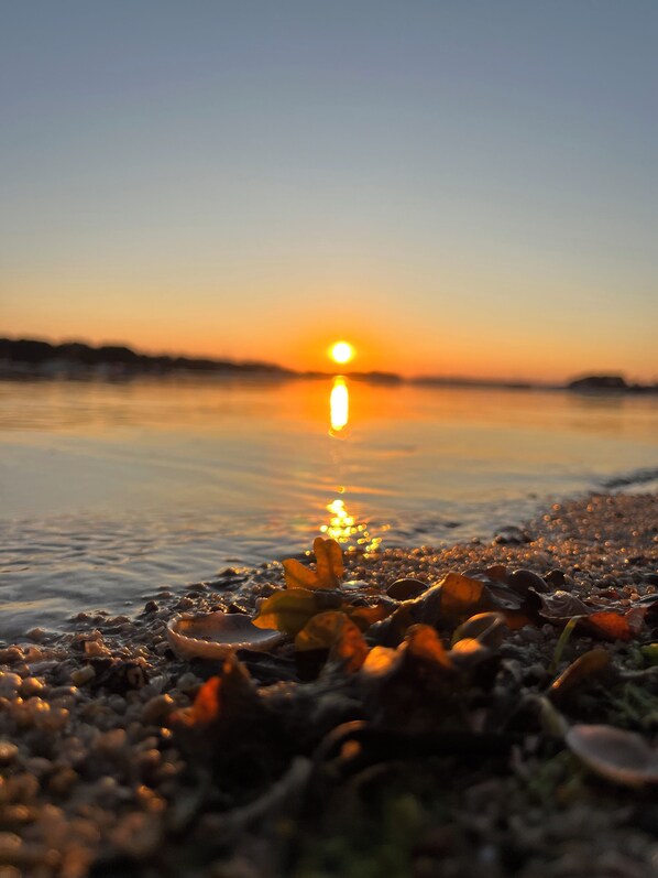 A sunset over a calm body of water with a beach in the foreground.