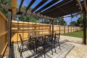 Un patio techado con cerramiento de madera, una mesa con sillas y una pérgola.