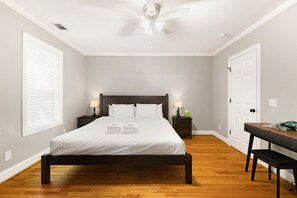 Un dormitorio ordenado con cama, mesitas de noche, escritorio y ventilador de techo.