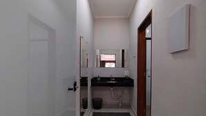 En smal hall som leder till ett badrum med handfat, spegel och en dörr.