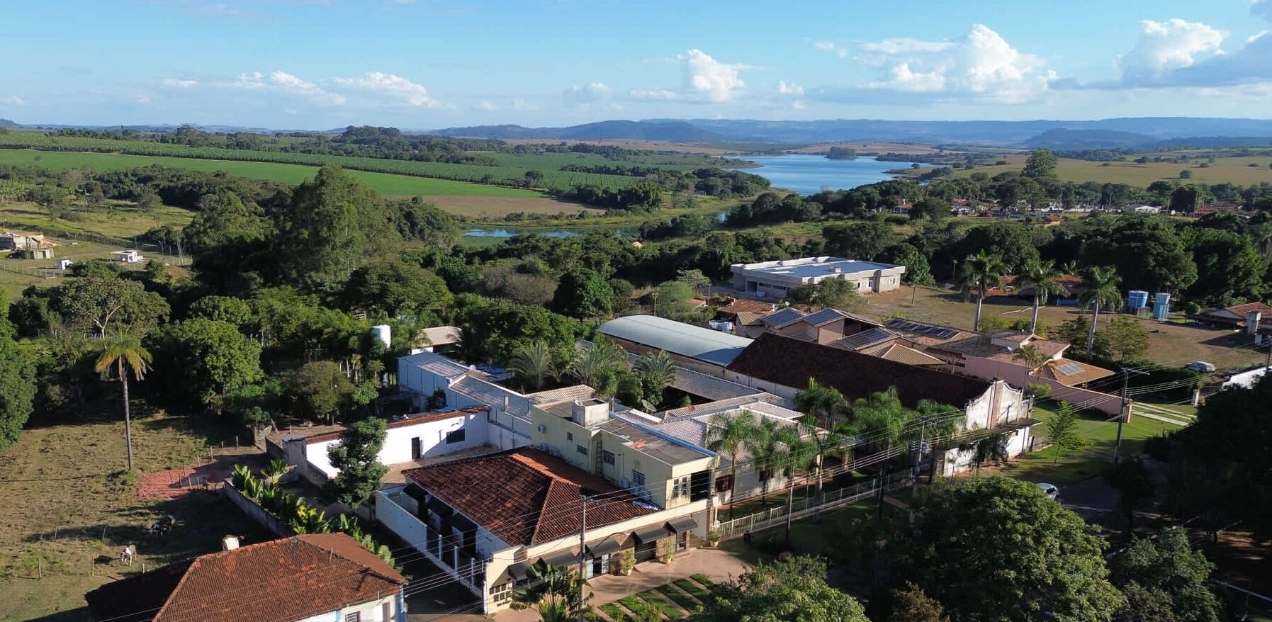 Une zone rurale avec une grande maison entourée de verdure et un lac en arrière-plan.
