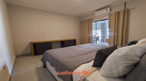 A bedroom with a bed, a bench, a window with curtains, and an air conditioning unit.