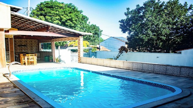 Una piscina con muelle de madera, un porche cubierto y un muro de ladrillo.