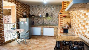 Una cocina compacta con salpicadero de ladrillo, estufa a gas, refrigerador y un pequeño comedor con mesa y sillas.