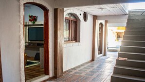 Un pasillo con suelo de baldosas, una puerta de madera y una escalera que sube a un nivel superior.