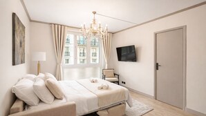 A bedroom with a bed, a chair, a TV, and a door. - 1600 Lecourbe (Paris)