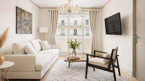 A modern living room with a sofa, a chair, a coffee table, a chandelier, a TV, and a window with curtains. - 1600 Lecourbe (Paris)