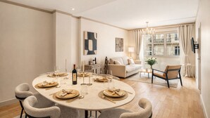 A dining area with a round table set for six, a sofa, a chandelier, and a window with curtains. - 1600 Lecourbe (Paris)