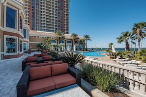 A hotel pool area with red cushioned seating, a clear view of the ocean, and a tall building in the background.