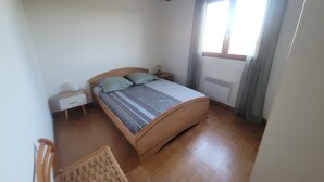 A bedroom with a wooden bed, a nightstand, a chair, and a window with curtains. - South Corsica house, close to the most beautiful beaches and mountains (Sotta)