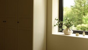 Une chambre dotée d’une grande armoire, d’une fenêtre donnant sur un paysage verdoyant et d’une petite plante en pot posée sur le rebord de la fenêtre.