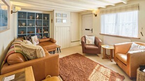 Una sala acogedora con un sofá de cuero marrón, una mesita redonda y una estantería llena de libros y objetos decorativos.