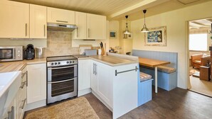 Cocina compacta con armarios blancos, horno integrado, cafetera y comedor con banco y mesa.