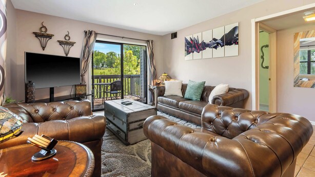 A living room with leather sofas, a flat-screen TV, and a balcony with a view.
