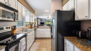A kitchen with white cabinets, stainless steel appliances, a granite countertop, and a view of the outdoors.