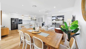 A modern kitchen with stainless steel appliances, a dining area with a wooden table and white chairs, and a large potted plant.