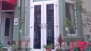 Un edificio con un letrero que dice "Ash Lea Hotel". Hay plantas en macetas y una mesa frente a la entrada.