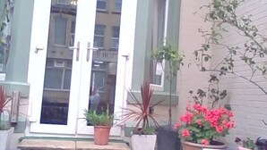 Exterior del Ash Lea Hotel con una entrada destacada, plantas en macetas y un banco al frente.