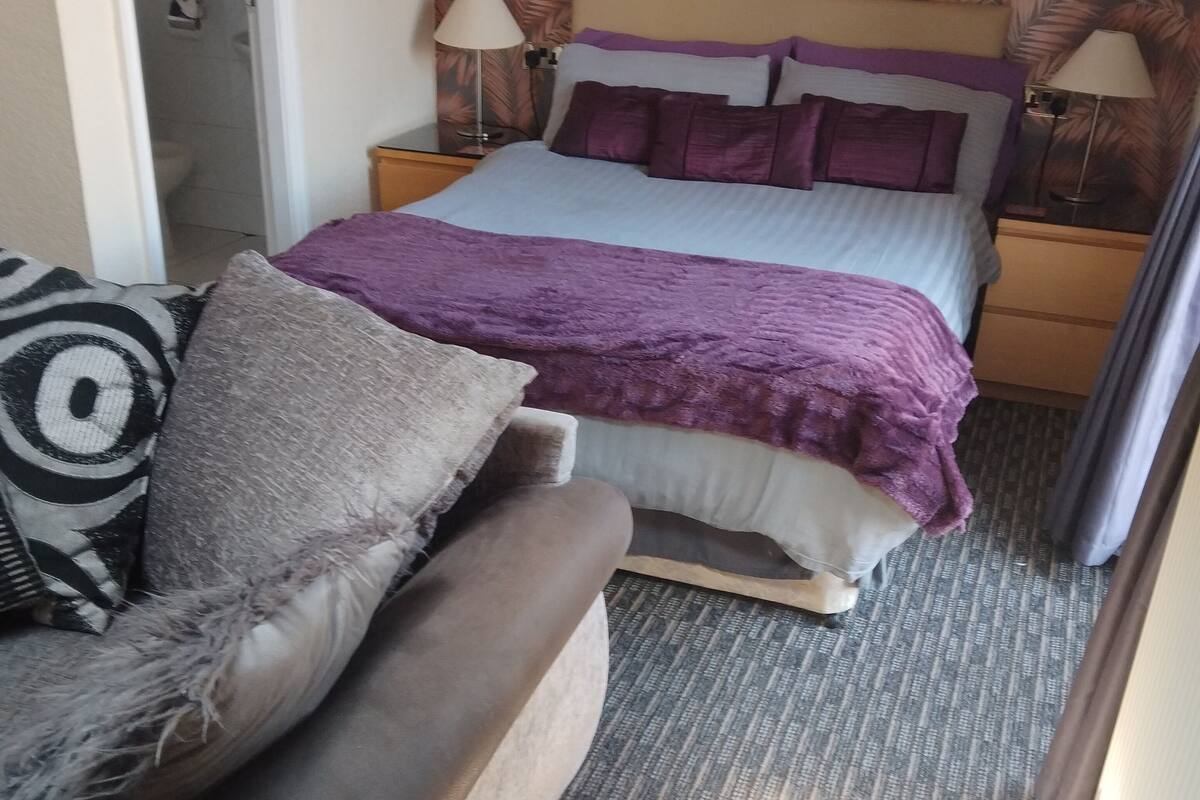 Um quarto com cama, sofá, mesa de cabeceira e abajur.