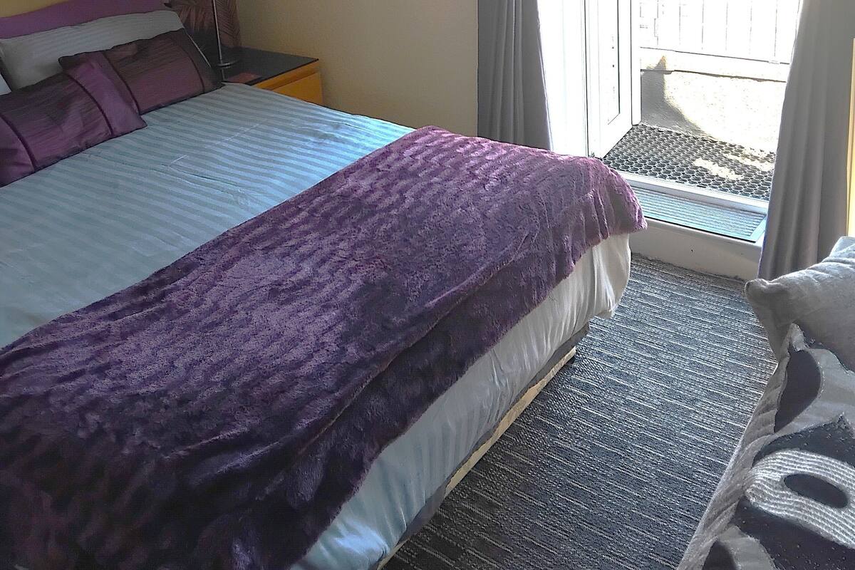 Quarto de hotel com cama, mesa de cabeceira, luminária, janela com cortinas e vista para o exterior.