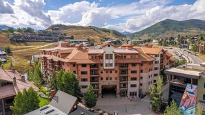 A multi-story hotel with a central entrance, surrounded by greenery and a mountainous backdrop.