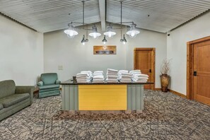 Una habitación con un mostrador de recepción amarillo, un sillón verde, una puerta de madera y una alfombra estampada.