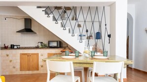 A kitchen with a dining area, wooden cabinets, a stove, and a staircase with hanging lights. - Holiday Home 'Barbara' with Private Garden, Wi-Fi and Air Conditioning (Teulada)