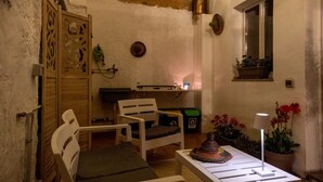 A cozy room with a wooden door, a white chair, a small table with a lamp, and a window with a view. - Holiday Home 'Barbara' with Private Garden, Wi-Fi and Air Conditioning (Teulada)